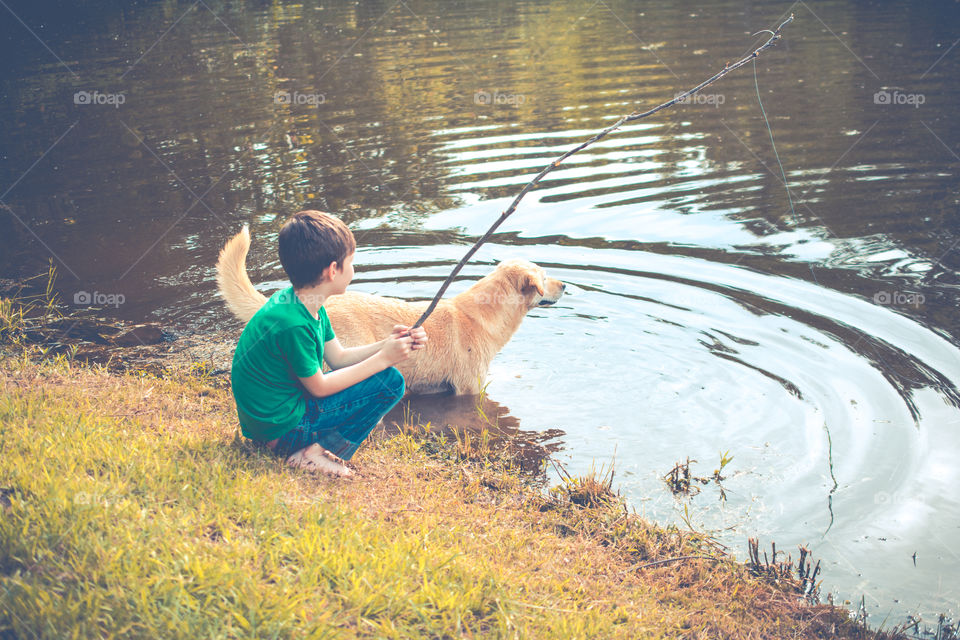 Young Boy Fishing at the Edge of a Pond with a Stick Pole and His Dog