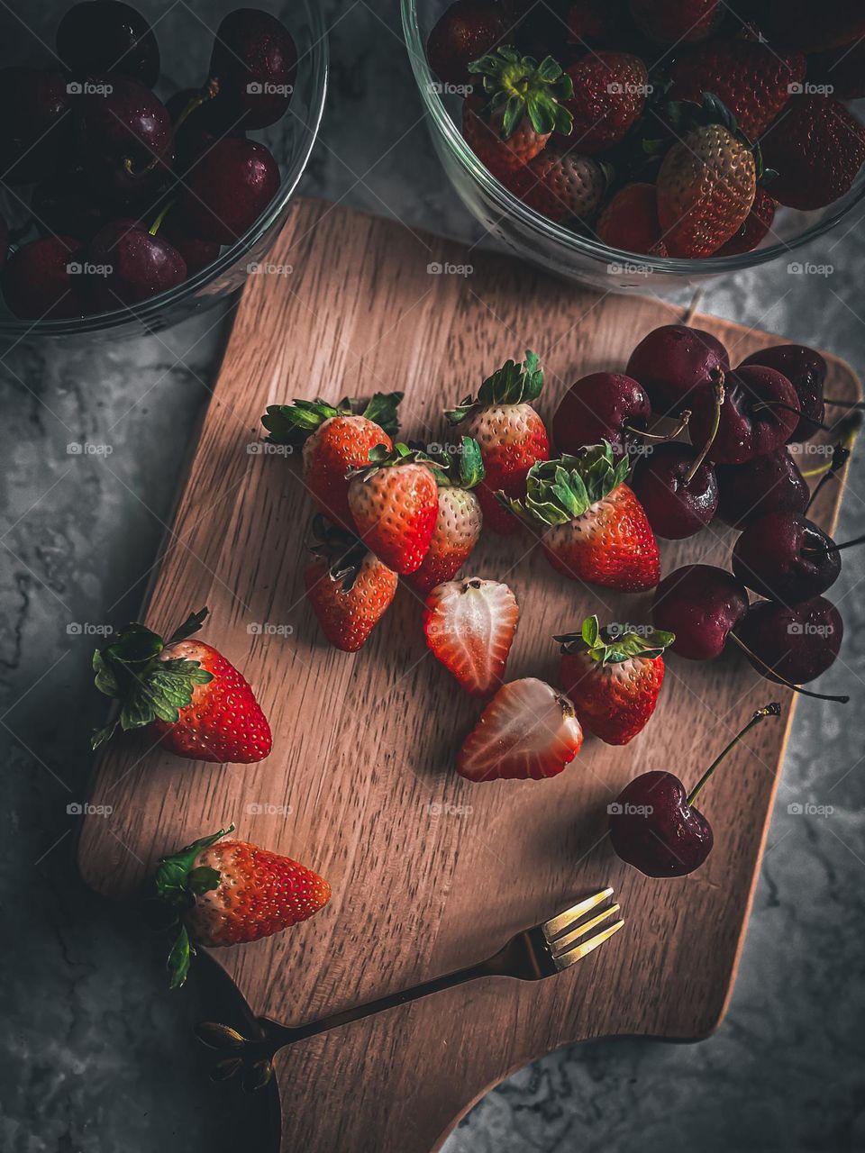 Fresh strawberries and cherries on top of a wooden cutting board 