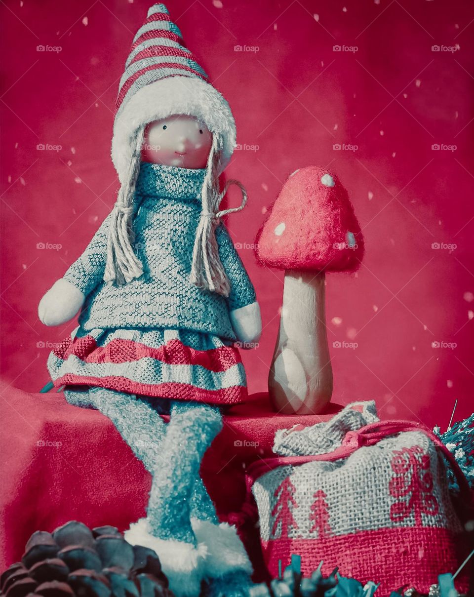 Christmasy doll in grey and red knitwear, sits against a magenta backdrop with a toadstool