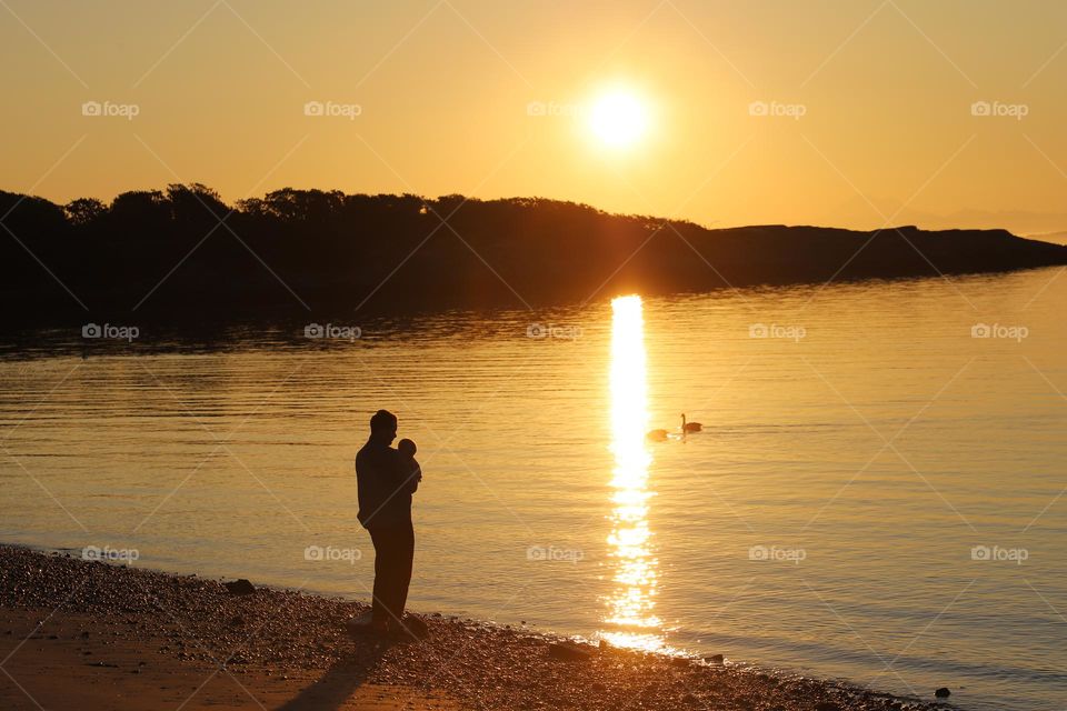 Man holding a baby by the beach , watching sunrise 