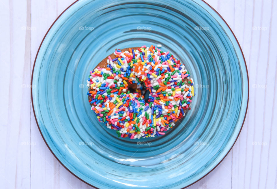 Flat lay of a round rainbow sprinkle donut on a round bright blue plate