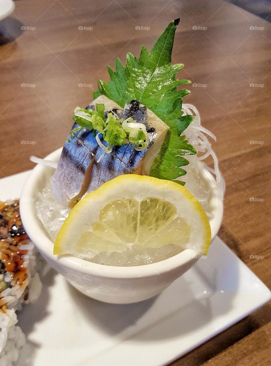 Mackerel Saba Sashimi over ice with lemon slice, shiso leaf, daikon radish, and green onion in a cup