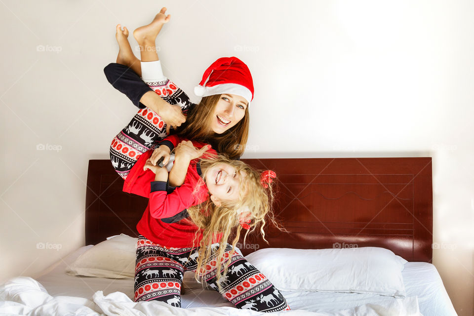 Holiday with family. Happy mother and daughter in Christmas pajamas playing on the bed