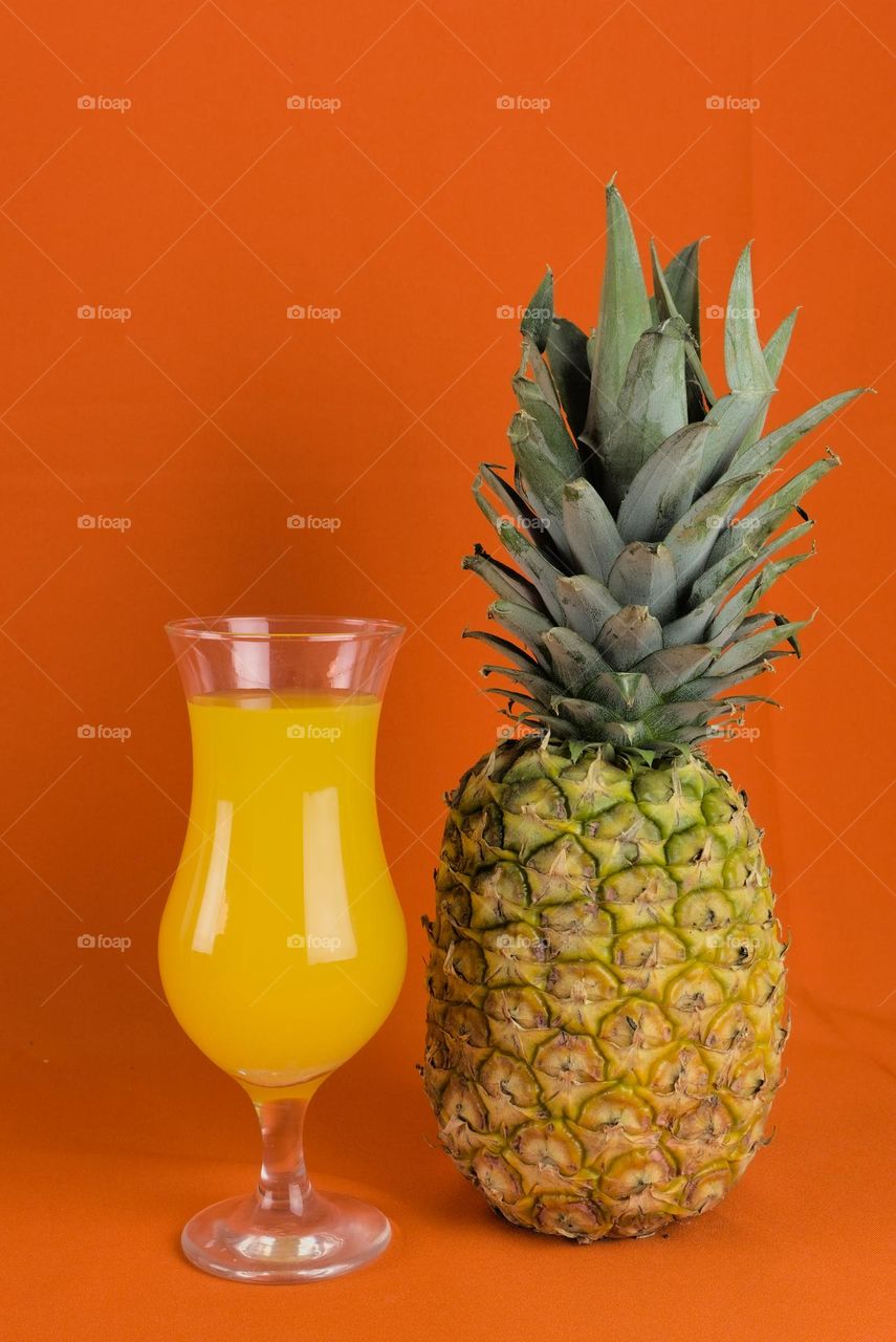 Pineapple with glass of natural juice on orange background