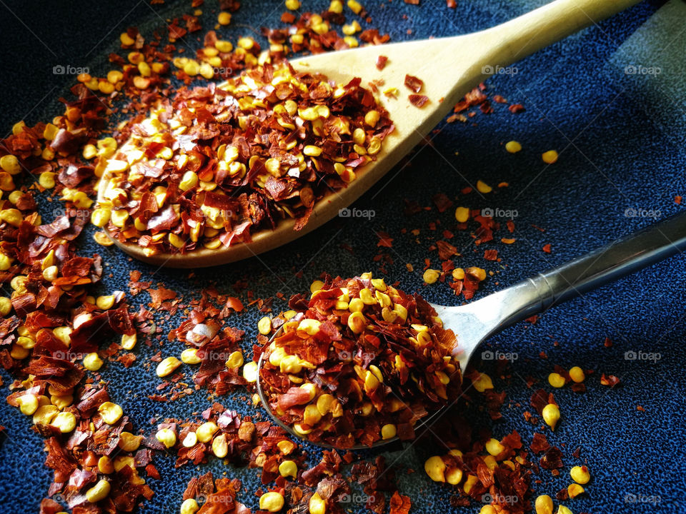 Dried red chili pepper flakes on wooden spoon and teaspoon.  Crushed chillies.