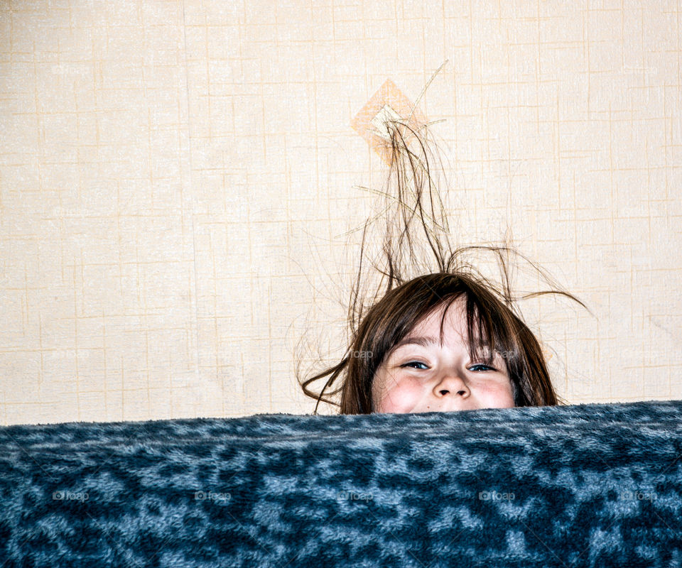 Laughing little girl hiding behind sofa