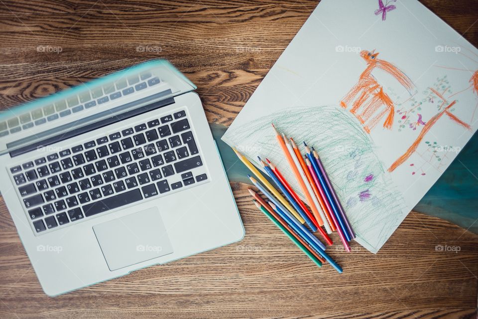 Children drawing with colorful pencils and laptop at wooden desk indoor