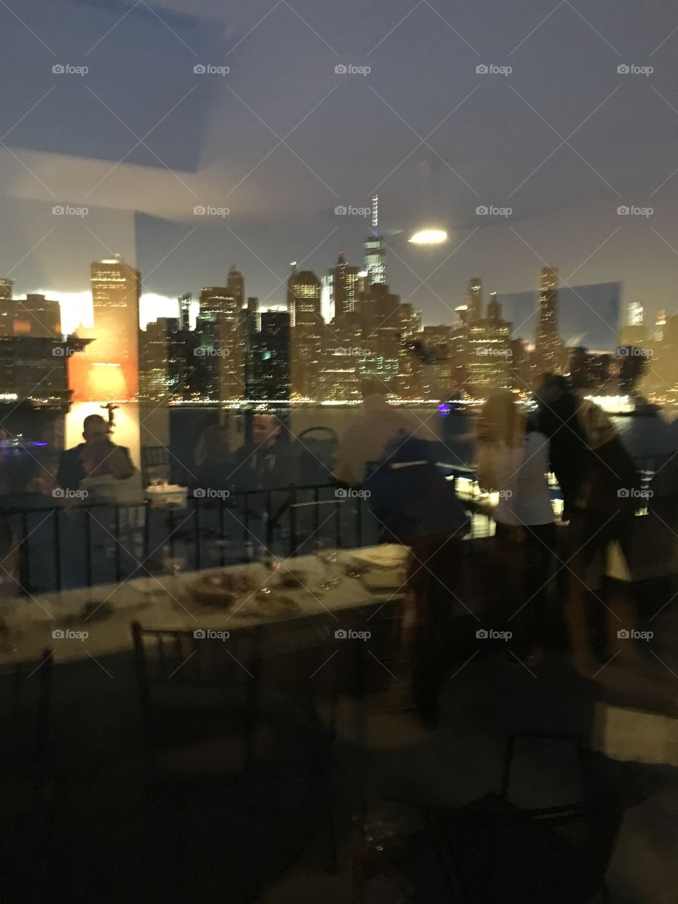 This luxury home “in the sky” on Pierrepoint Place in Bklyn, NY has breathtaking views from the balconies. The Manhattan skyline and the Empire State reflect in the window and the dinner guests can be seen through the glass. 2017 Hypnotic Productions