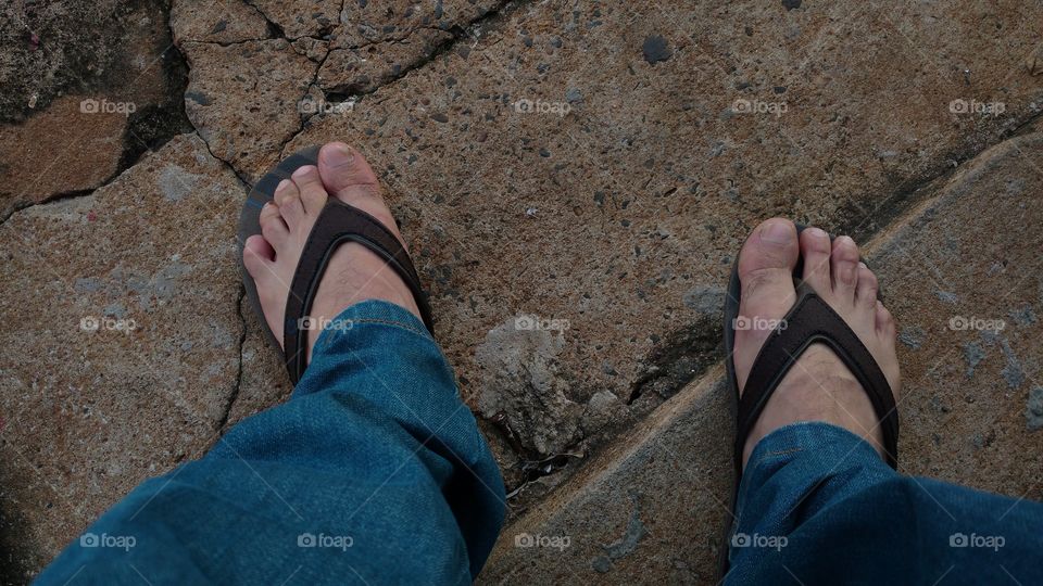 Pés com chinelos na calçada.