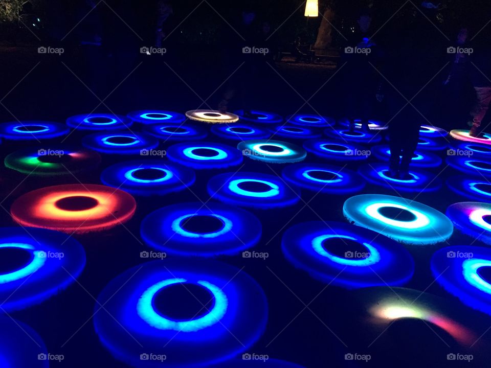 Glowing blue circles in a pattern on the ground. There are a few in other colors scattered among them. Someone is standing on one of them. 