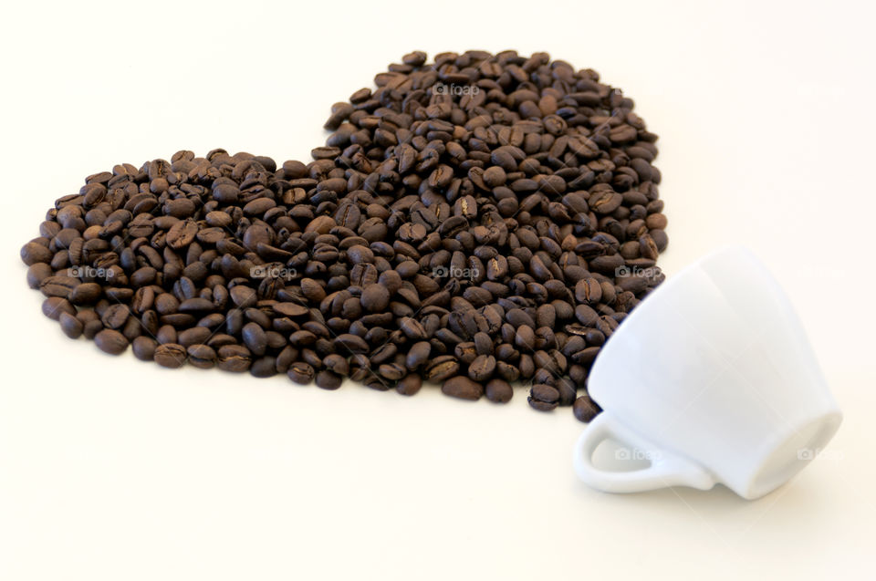 Coffee beans poured out of small cup on light background