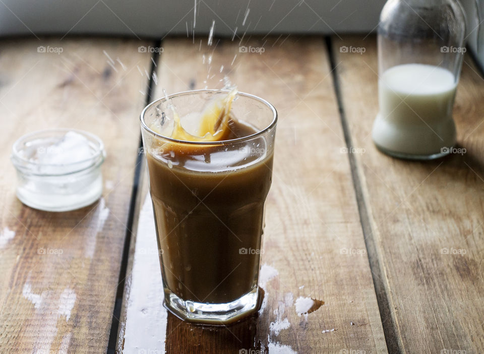 Iced coffee with splashes on wooden table