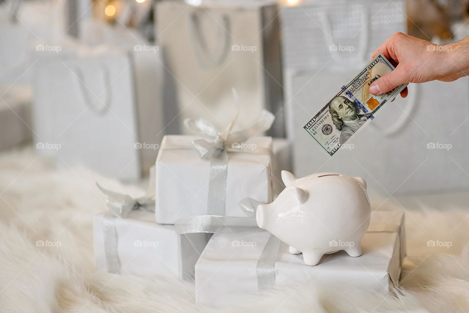 piggy bank with 100 dollars banknote in festive New Year atmosphere of scenery.  Magical bokeh with Christmas tree and bright lights.