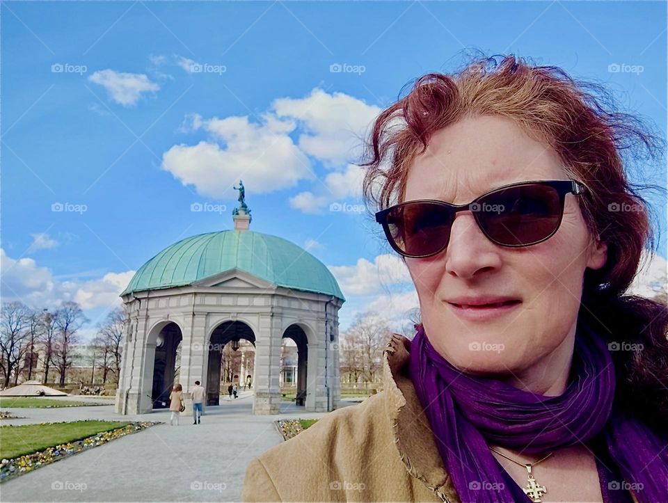 The young lady is in the “Hofgarten” or “Court Garden” in “Munich”, capitol of “Bavaria”, Germany. The pavilion like structure is a temple to “Diana” in-midst of a garden with geometric star shaped walkways. 2024. Hypnotic Productions