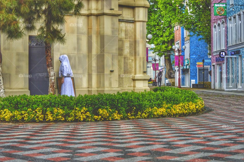 a nun enters the church near a flower bed with yellow flowers