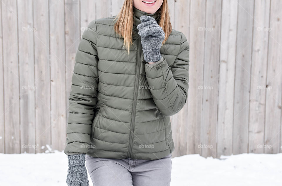 Close-up of a young woman zipping up her winter coat outdoors in the snow