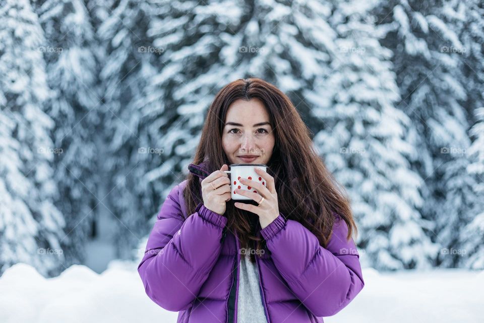 Happy woman drinking hote tea while on a day trip in the mountains in winter.