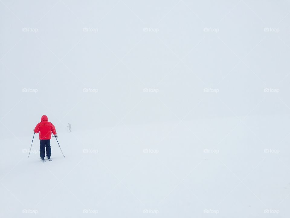 Skier in red ski jacket surrounded by fog and snow