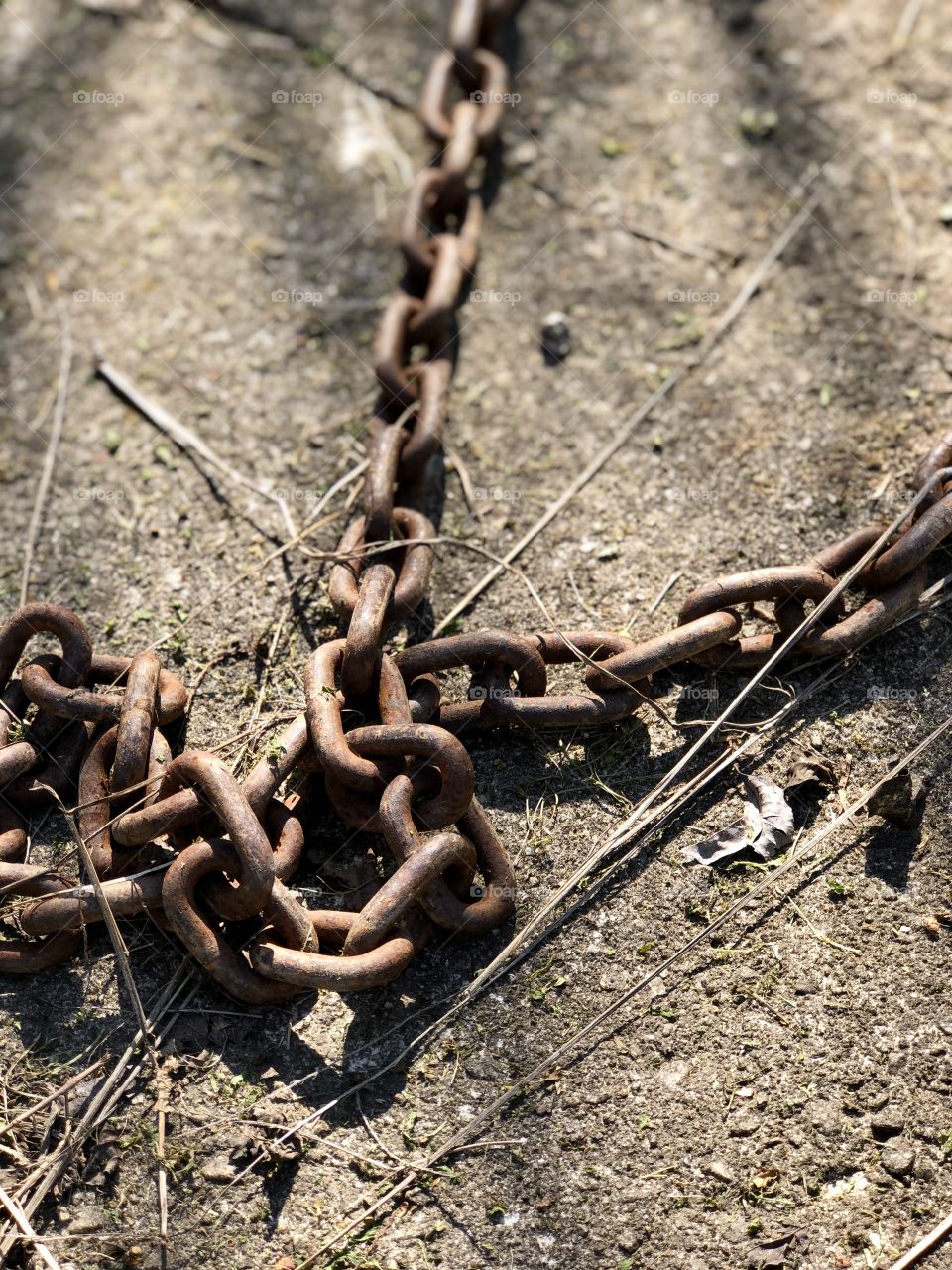 Old rusted heavy chain lying on concrete slab in sun and shadows 