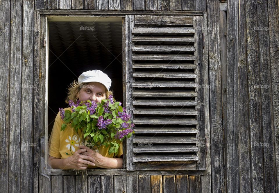 A woman on country house window, holding lilac flowers