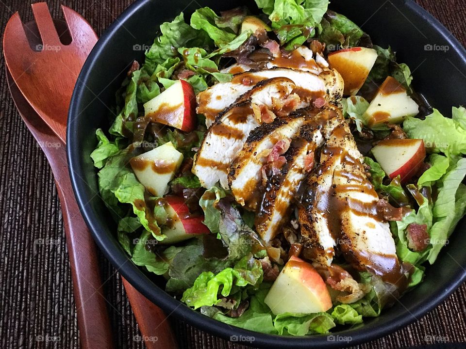 Salad topped with grilled chicken, chopped apples, bacon bits and balsamic salad dressing