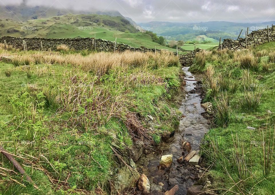 A small stream flows through a green and hilly landscape 