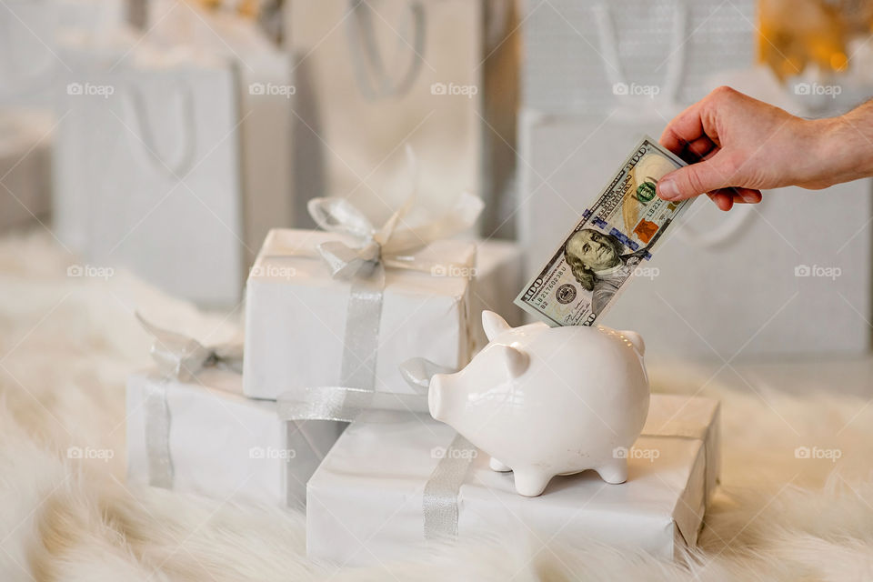 piggy bank with 100 dollars banknote in festive New Year atmosphere of scenery.  Magical bokeh with Christmas tree and bright lights.