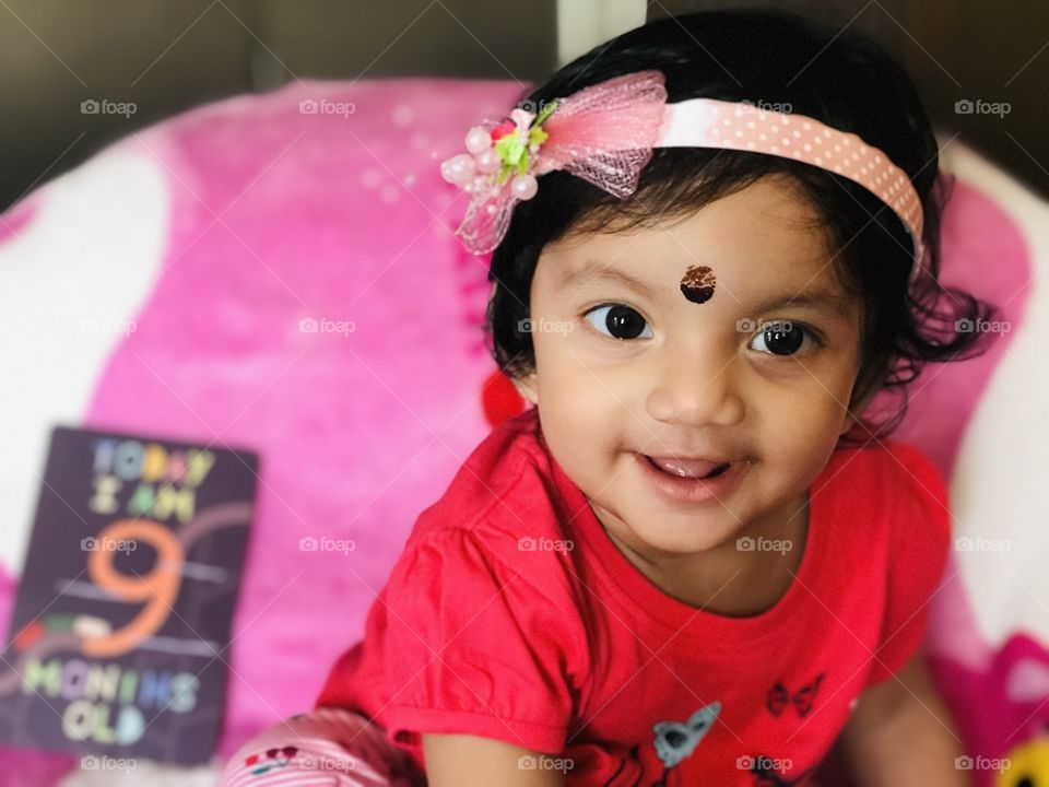 Indian baby girl with pink hair band and black bindi on forehead 