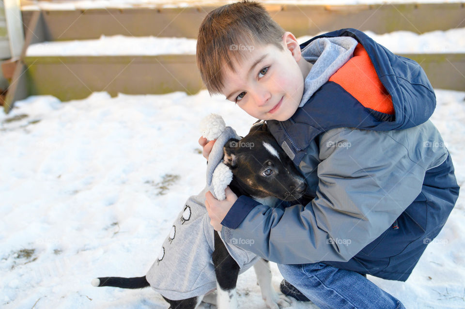 Young boy hugging his new puppy in the snow during winter