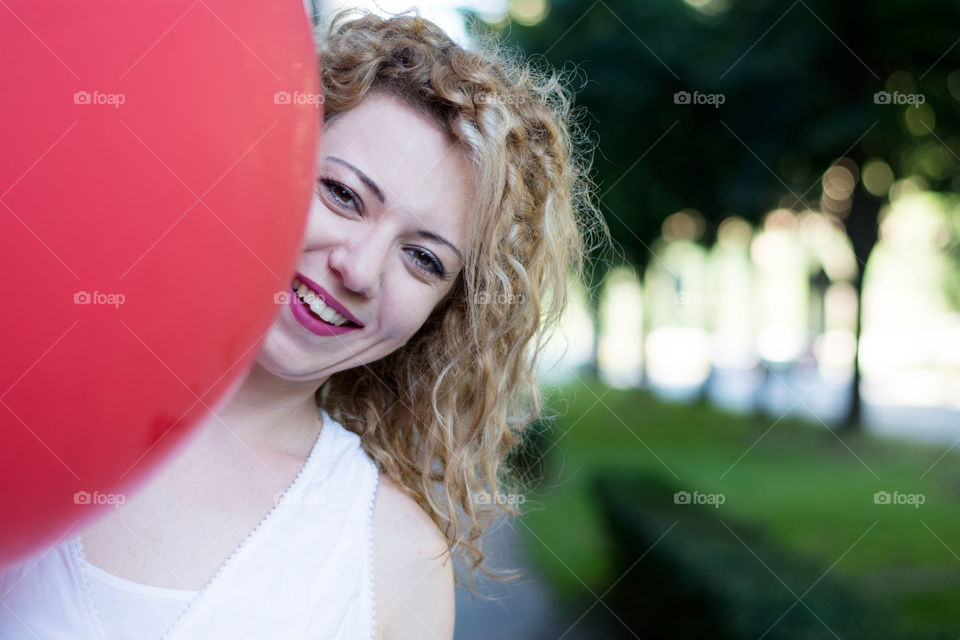 girl behind big red balloon. curly blond girl smiling behind a big red balloon