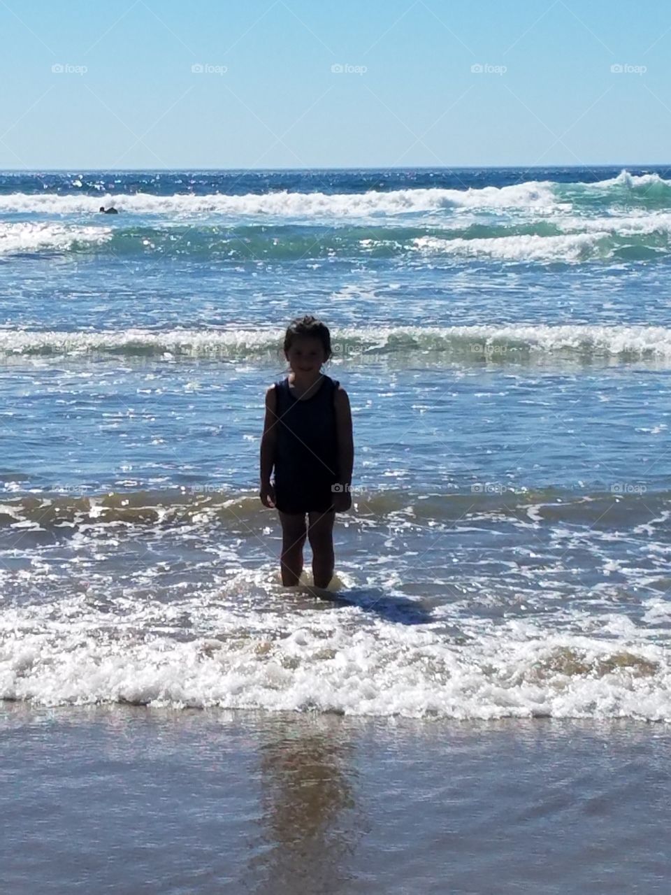 Little girl's silhouette contrasts against sparkling Pacific Ocean.