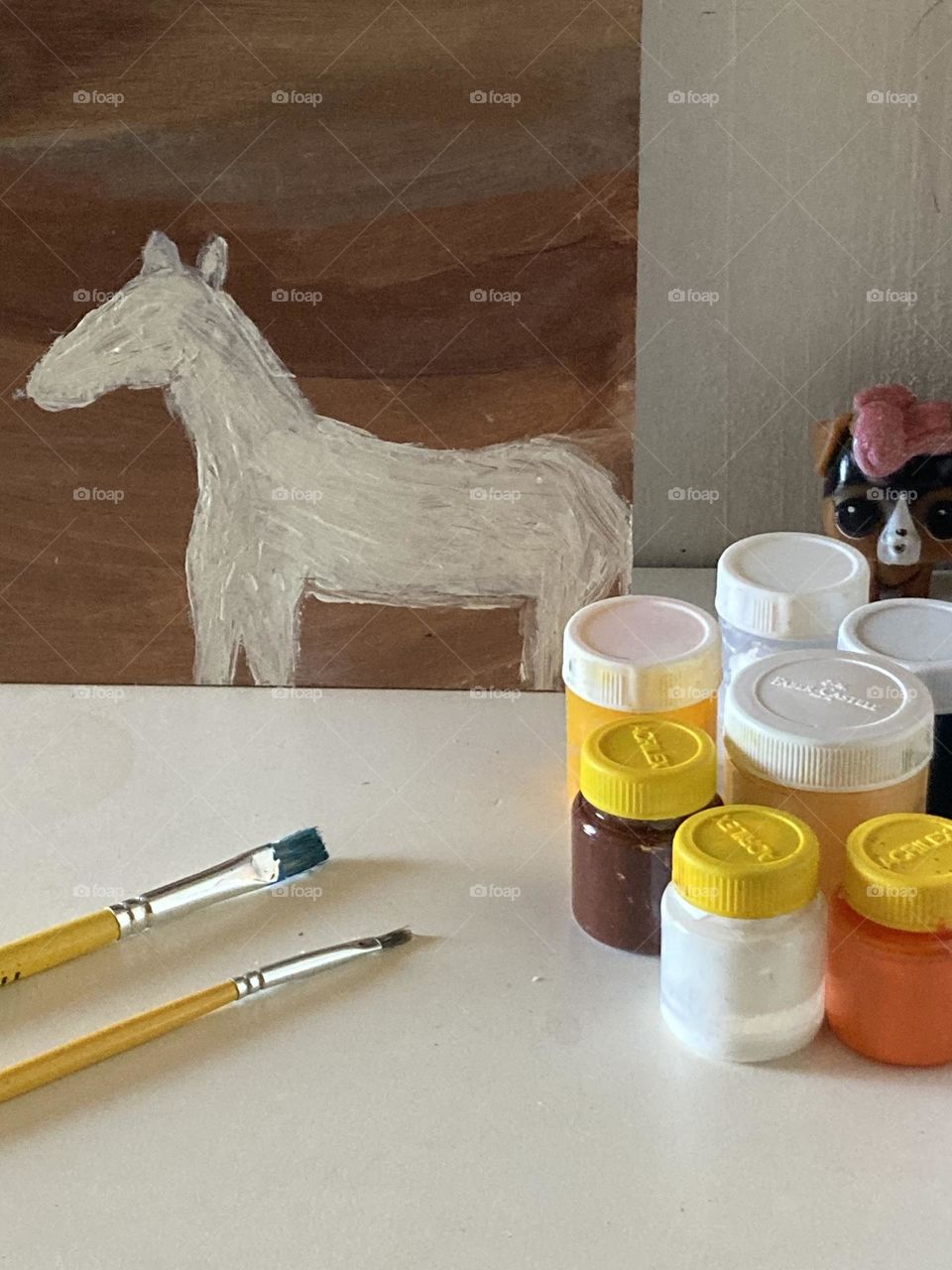 Mesa da adolescente para realizar pintura de quadrinhos. Sobre a mesa quadro de pintura e materiais como tintas e pincéis.