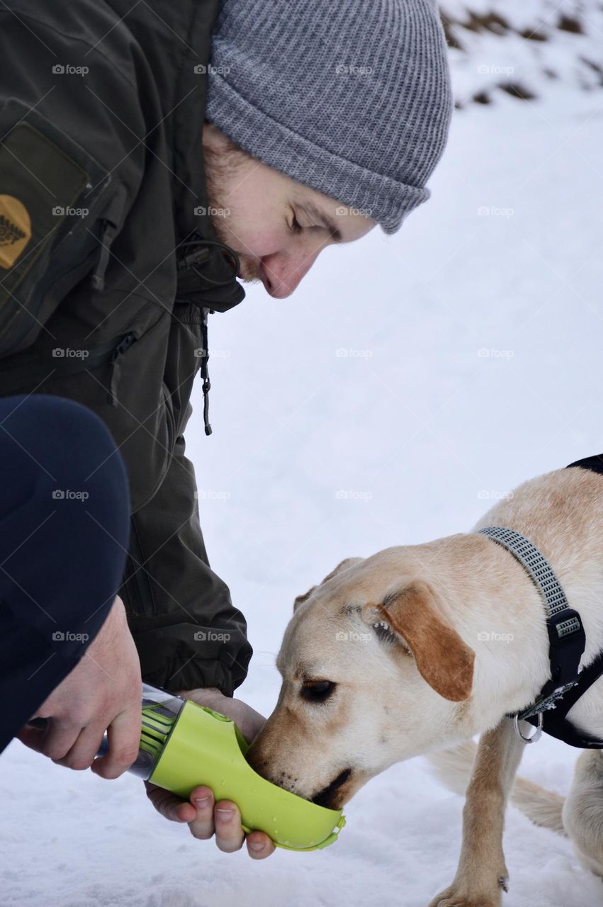 Young man giving a dog water in winter