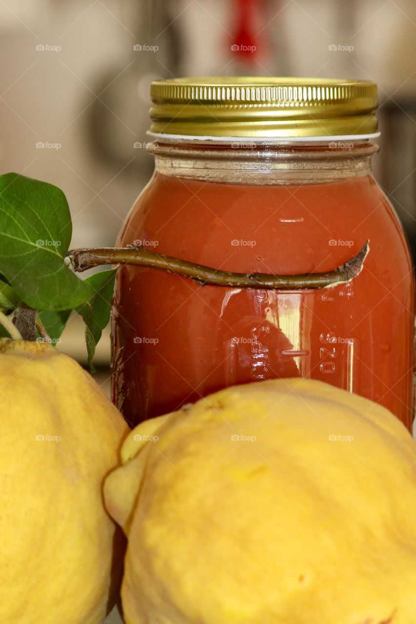 Closeup ripe quince fruit on branch with canned jar quince preserves foreground and blurred kitchen background