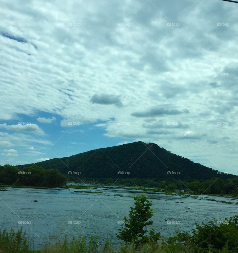 Beautiful hill with water at the base of it with a cloudy sky.,