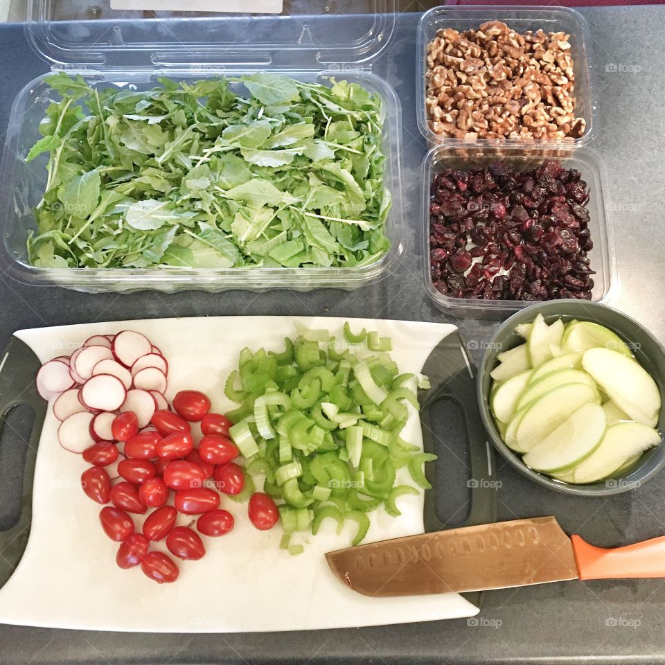 Meal prepping a healthy salad with fresh green apples, mixed greens, dried cranberries, cherry tomatoes, radish, celery and walnuts. 