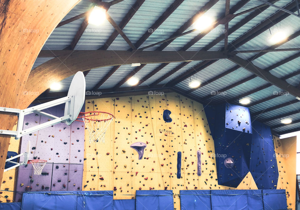 A brightly, lit public gymnasium with basketball hoops and a climbing wall, in France