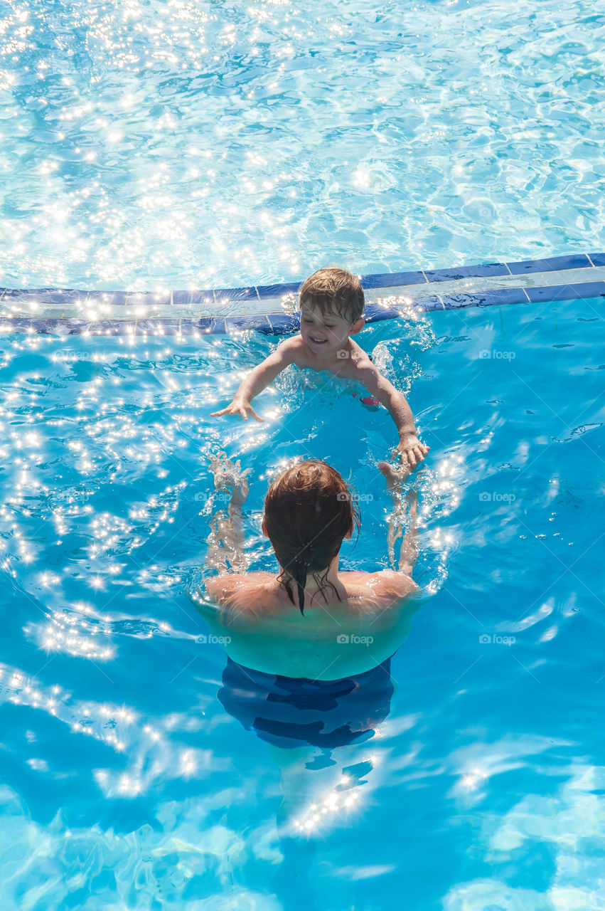 Mother encoraging her little son into the swimming pool.