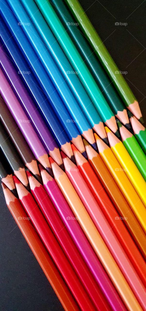 Colourful flatlay on black surface of a double alignment of colored pencils with their mines interlocked