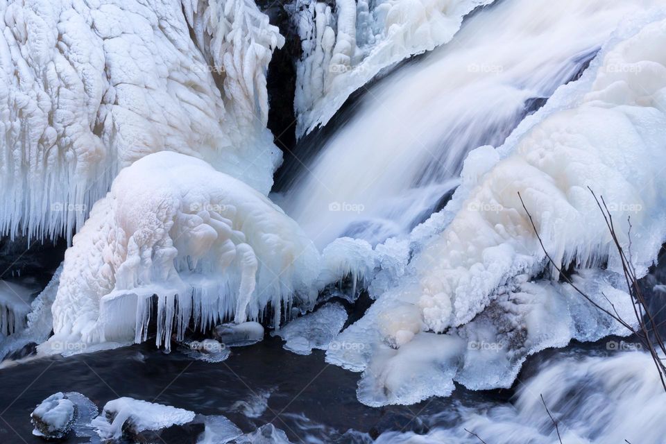  Rocks covered with beautiful white ice and icicles in a strong stream with running water on a cold winter day 