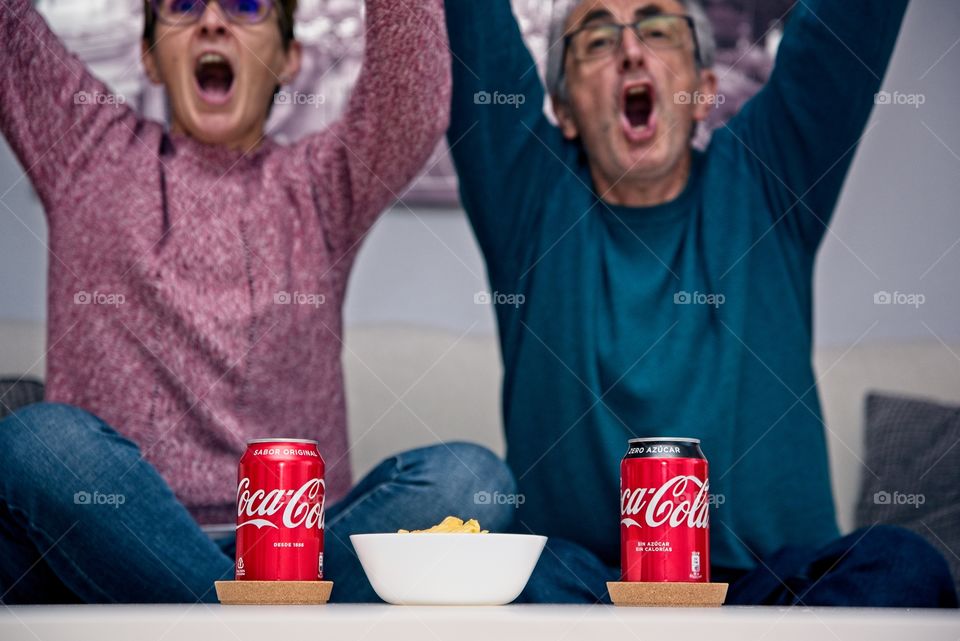 Couple eating a snack with Coca Cola while watching football