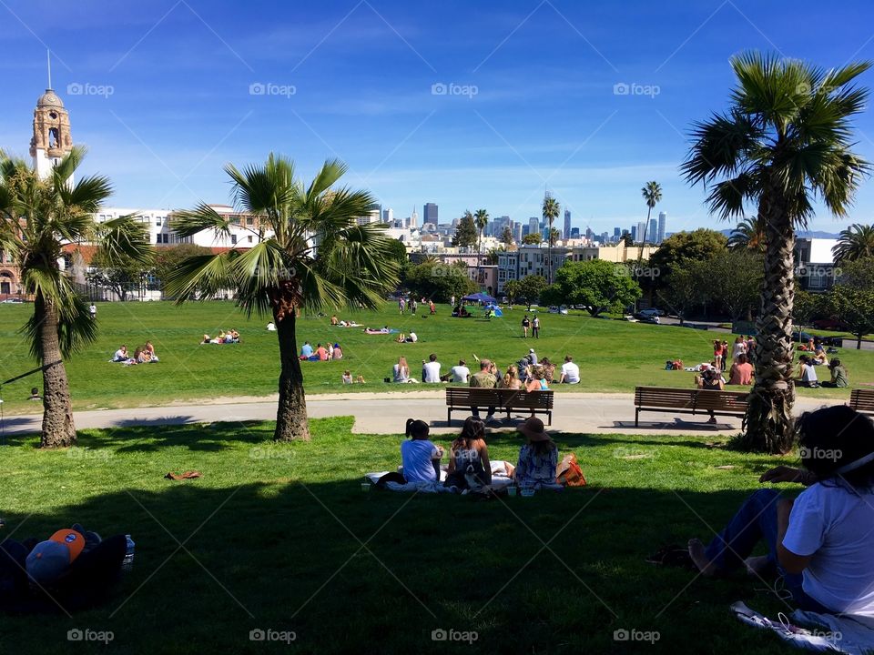 People chill on top of the hill at Mission Dolores Park, the San Francisco city skyline is seen in the distance. 