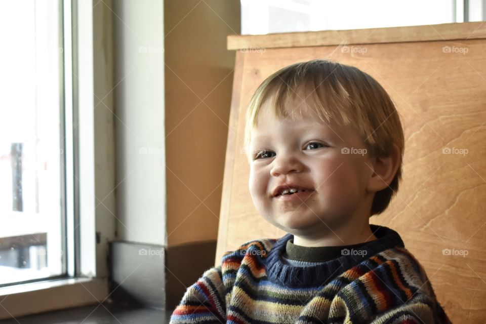 Cute 19 month toddler boy in colorful sweater having fun at dinner table 