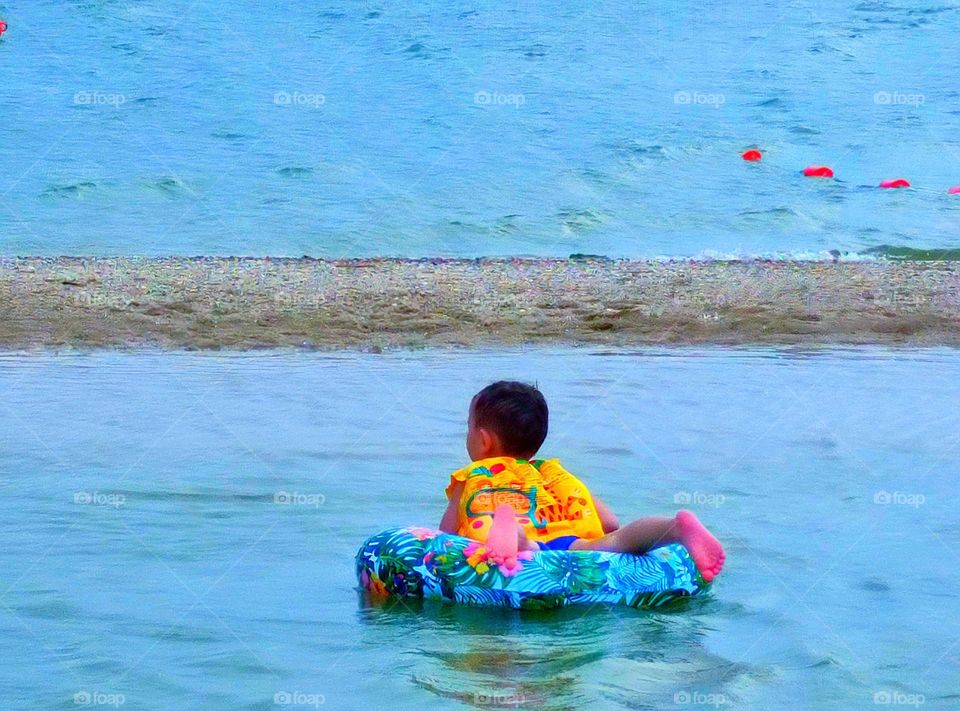 Seashore after low tide. A boy floats on a water mattress in warm coastal water
