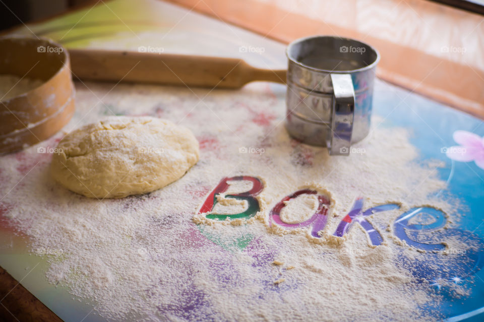 On the table lies a pastry for pies with sprinkled flour and a seeder for flour. Written to bake on the table.
