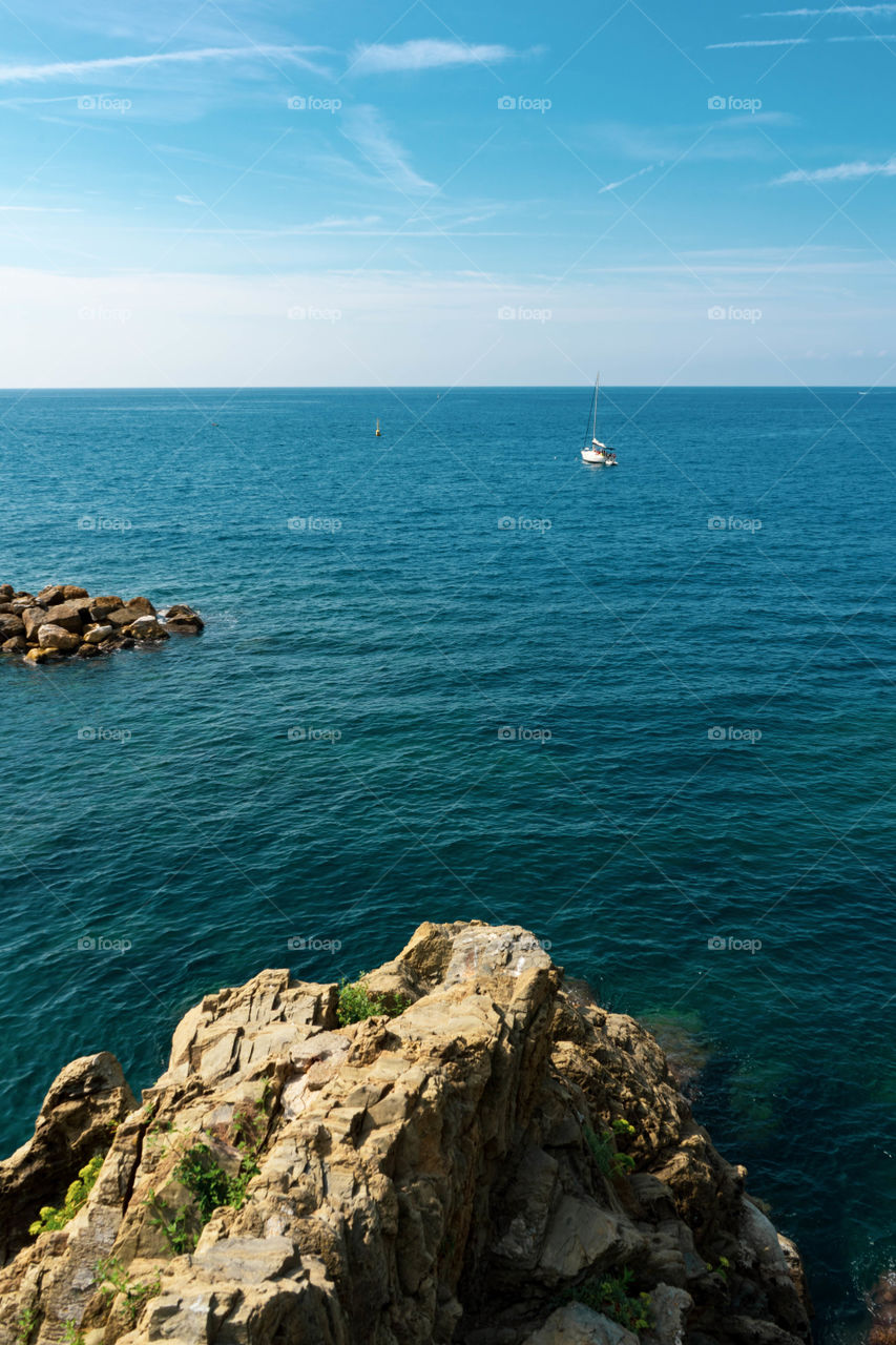 The sea view from the Cinque Terre. The boats sail between the waters and the rocks. A small house overlooking the sea colors the view.