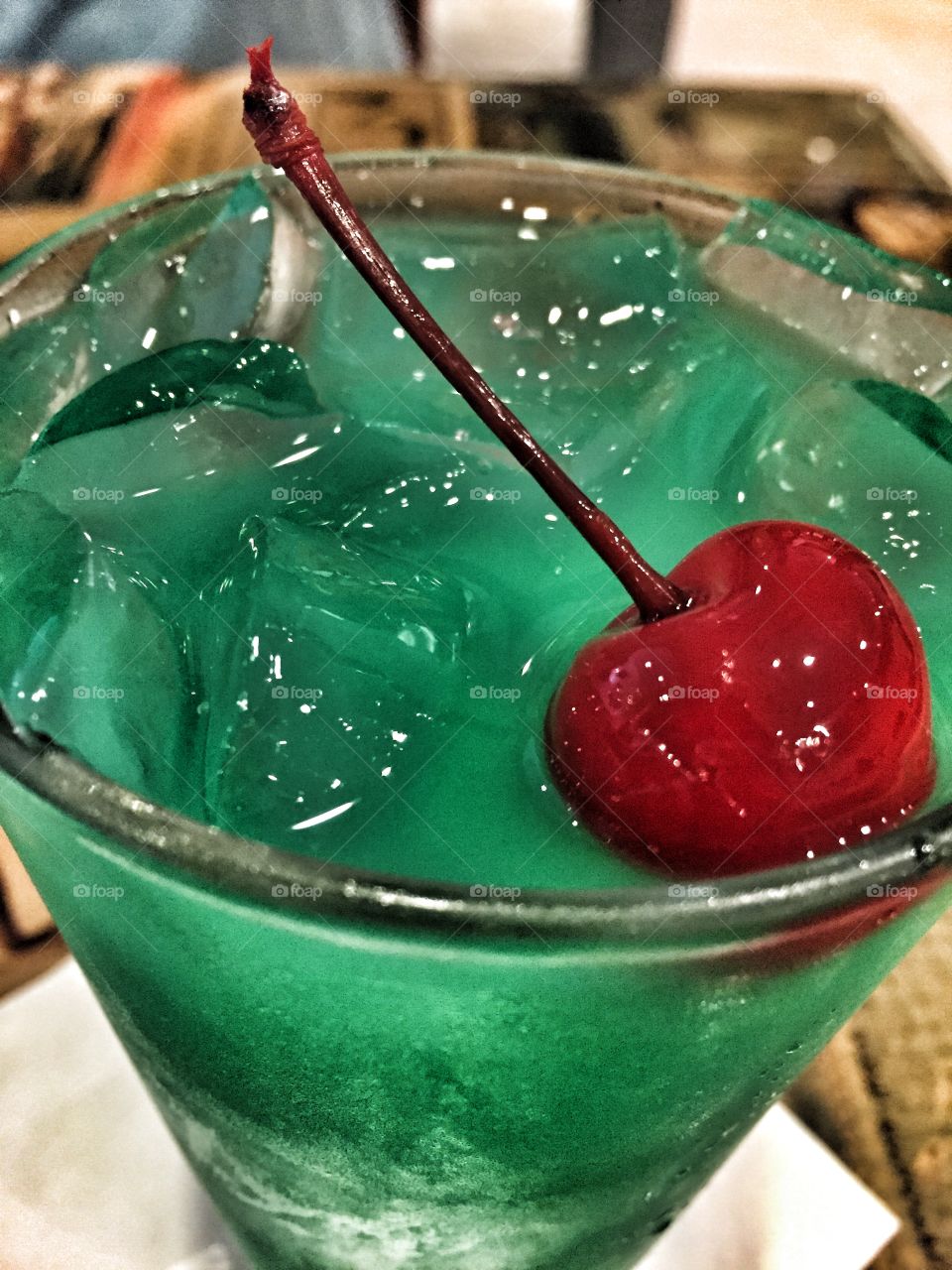 Bright red cherry in a green cocktail with ice cubes