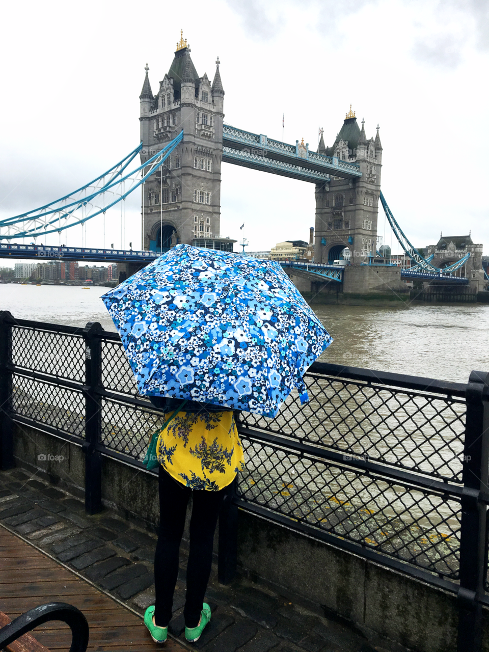 A blue floral umbrella contrasting with a yellow blouse. In front of the Tower of London bridge