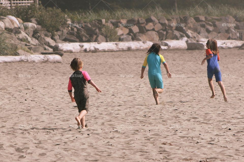 Three sisters racing down the beautiful, sandy beach playing tag and enjoying the hot sun on a beautiful summer day. 