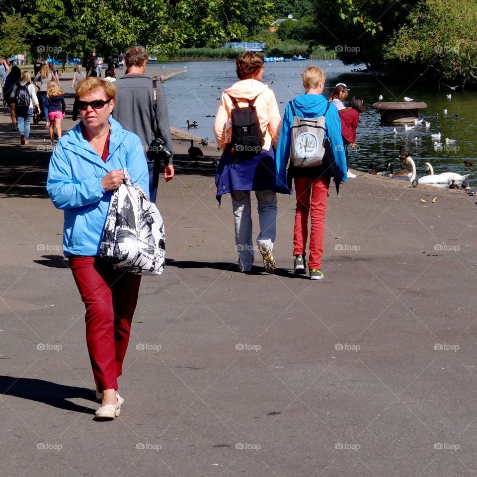 People walking on a path along the waterfront of an urban park on a sunny summer day. 